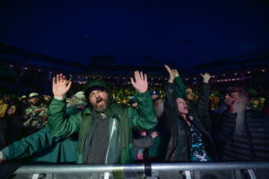 Crowd at a nighttime concert pressed against the barrier, front-row fans cheering with raised hands.