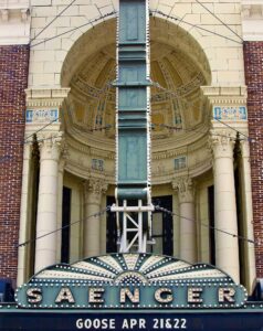 Historic theater façade with an ornate arch, columns, and a vertical green marquee showing Goose performances on Apr 21 & 22.