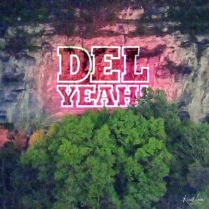 Large pink graffiti letters outlined in white on a weathered wall, with an artist's signature in the bottom-right corner.