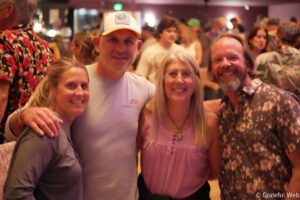 Three friends posing for a selfie at a lively indoor gathering, smiling at the camera with others mingling in the background.