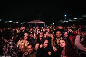 Crowd of concertgoers at night, smiling and posing for the camera with a canopy tent in the background.