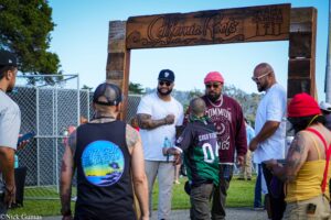 Group of people chatting under a large wooden arch at an outdoor event.