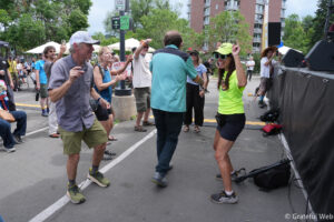 People dancing and cheering at an outdoor street festival with a stage on the right.
