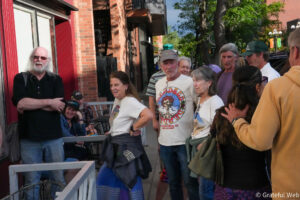 Group of adults standing and chatting on a sunny city sidewalk beside a brick building.