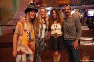 Four friends posing together in a colorful venue, smiling at the camera and enjoying a night out with vibrant walls behind them for context.
