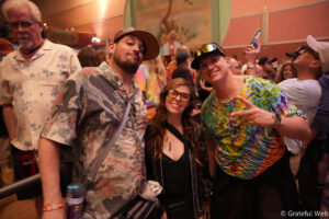 Group of friends at a party posing for a photo; three people in colorful tropical shirts and smiles.