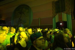 Crowd of people in a dimly lit indoor venue, faces illuminated by green stage lights during a performance.