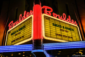 Close-up of a red neon sign on a vintage theater marquee lit by bulbs at night.