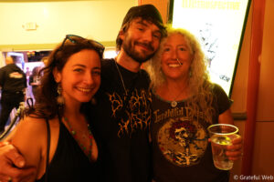Three friends posing closely at a party, smiling at the camera with drinks in hand.