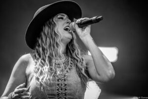 Female singer wearing a wide-brim hat performs on stage, gripping a microphone.