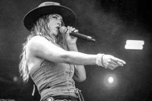 Female singer performing on stage with a microphone, wearing a wide-brim hat and denim outfit (black-and-white).