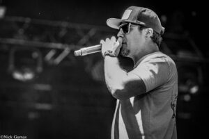 Male singer in a cap and sunglasses performs on stage, microphone near his mouth (live performance).