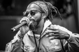 Black-and-white image of a male singer wearing a patterned bandana and sunglasses, singing into a microphone.