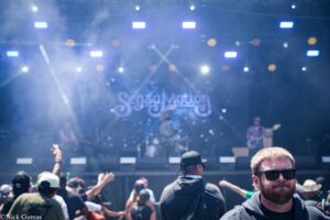 Crowd at a concert in front of a foggy stage with blue lights and musicians performing.