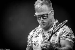 Bearded guitarist wearing sunglasses and a tropical shirt, playing a guitar on stage (black and white).