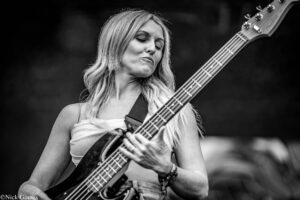 Female bassist performing on stage, close-up of her face and hands on the bass guitar neck, black-and-white image.