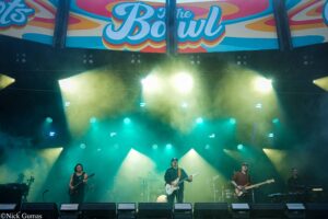 Colorful outdoor concert stage with a band performing under a bright, bannered backdrop and foggy lights