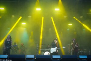 Live rock band on stage performing under bright yellow spotlights with smoky atmosphere.