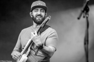 Guitarist with a beard and cap playing an electric guitar, eyes closed, on stage (black-and-white photo).