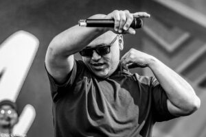 Male singer wearing sunglasses performs on stage, gripping a handheld microphone above his head.