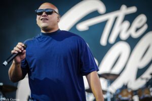 Male singer on stage wearing a blue shirt and sunglasses, holding a microphone.