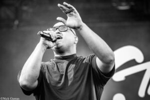 Male singer on stage, microphone in hand, one arm raised in performance (black-and-white concert shot).