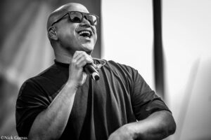 Bald male singer wearing sunglasses, holding a microphone and singing on stage (black-and-white photo).