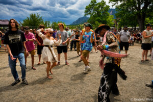 Group of people dancing outdoors at a festival, with mountains and cloudy sky in the background.