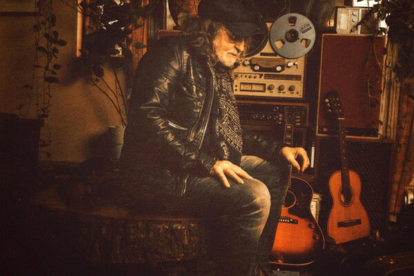 Album cover image: Ray Wylie Hubbard seated in a cozy studio with reel-to-reel gear and guitars, in a warm vintage tone; title text reads 'RAY WYLIE HUBBARD' at top and 'REEL 2 REEL 4 REAL' at bottom