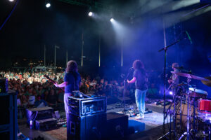 Band performs on a lit stage at night as a large crowd watches from the festival grounds.