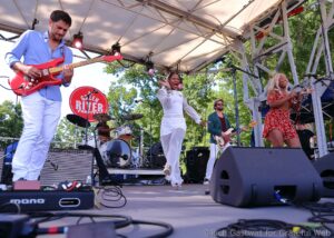 Live band on an outdoor stage at Green River Festival: guitarist left in blue shirt, two female singers center and right, drummer in back.