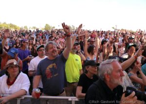 Large crowd at an outdoor concert with hands raised toward the stage.