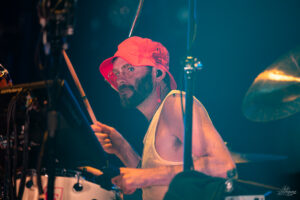 Drummer with a red bucket hat and glasses playing a drum kit on stage.