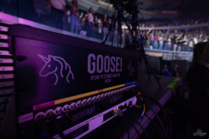 Goose! FOH video rack with unicorn logo, cables in foreground, audience visible in a dark arena behind.