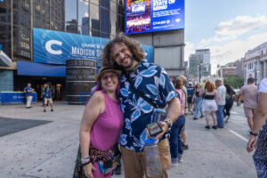Smiling couple posing on a city street at a Chase Madison Square Garden event, with a blue banner behind them on a modern building exterior.
