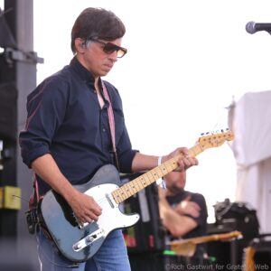 Male guitarist wearing sunglasses and in-ear monitors, playing a blue Fender Telecaster on stage during a performance.