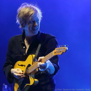 Guitarist playing a yellow electric guitar on a blue-lit stage during a live performance