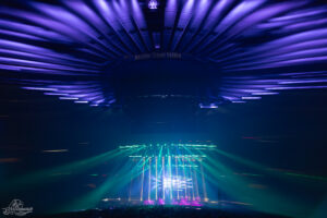 Concert stage at Madison Square Garden with vivid purple ceiling lights and green laser beams piercing the arena.