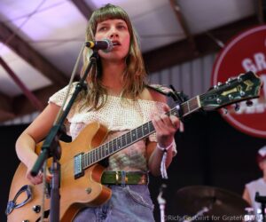 Young woman singer playing an acoustic guitar on stage, singing into a microphone.