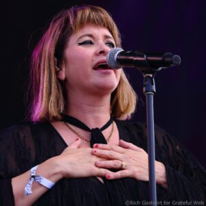 Female singer on stage singing into a microphone with hands pressed to her chest.