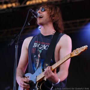 Male guitarist singing into a microphone while playing an electric guitar on stage.