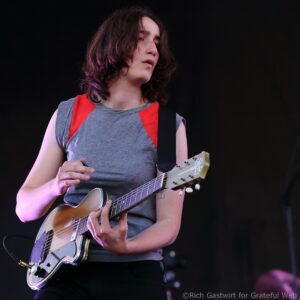 Young guitarist performing on stage, focused on playing a steel-string guitar with a red and gray outfit.