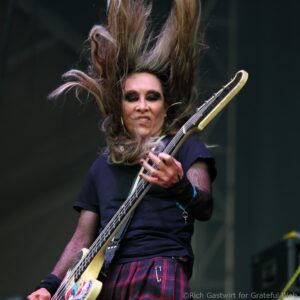 Female bassist performing on stage with windblown hair while playing a guitar bass.