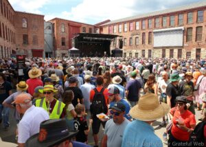 Large crowd gathers in a brick-walled courtyard for an outdoor concert, with a stage and band performing at the center.