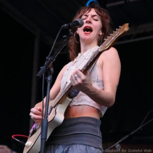 Woman singer passionately performs into a microphone while playing an electric guitar on stage.