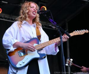 Female musician singing into a microphone while playing a sunburst Fender Telecaster on stage.