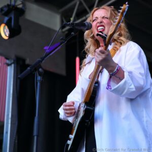 Female singer-guitarist performing on stage, gripping a guitar and singing into a microphone.