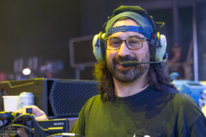 Male audio technician wearing a headset with mic at a control station, smiling at the camera during a live event