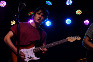 Guitarist performing on stage with a sunburst Fender Stratocaster under colorful stage lights