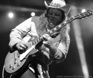 Guitarist wearing a cowboy hat playing an electric guitar on stage in black and white.